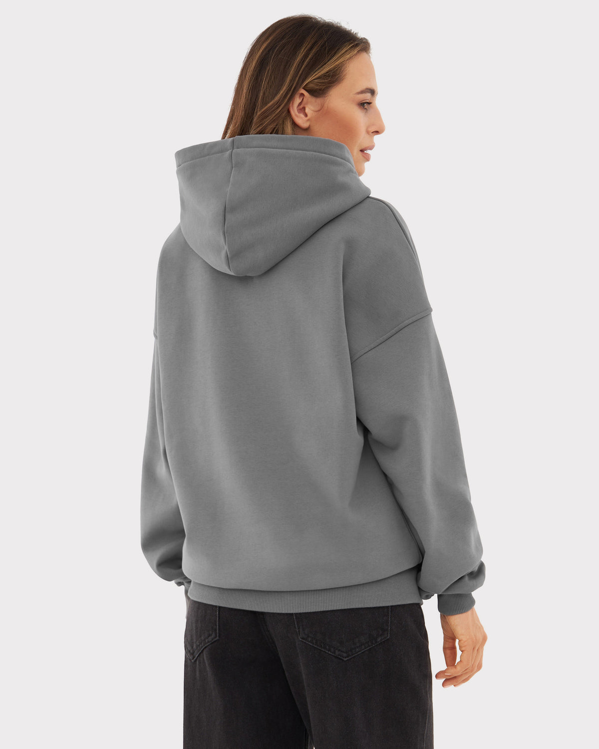Rückansicht einer Frau mit oversized Hoodie 'Cody' in Grau, kombiniert mit schwarzen Hosen