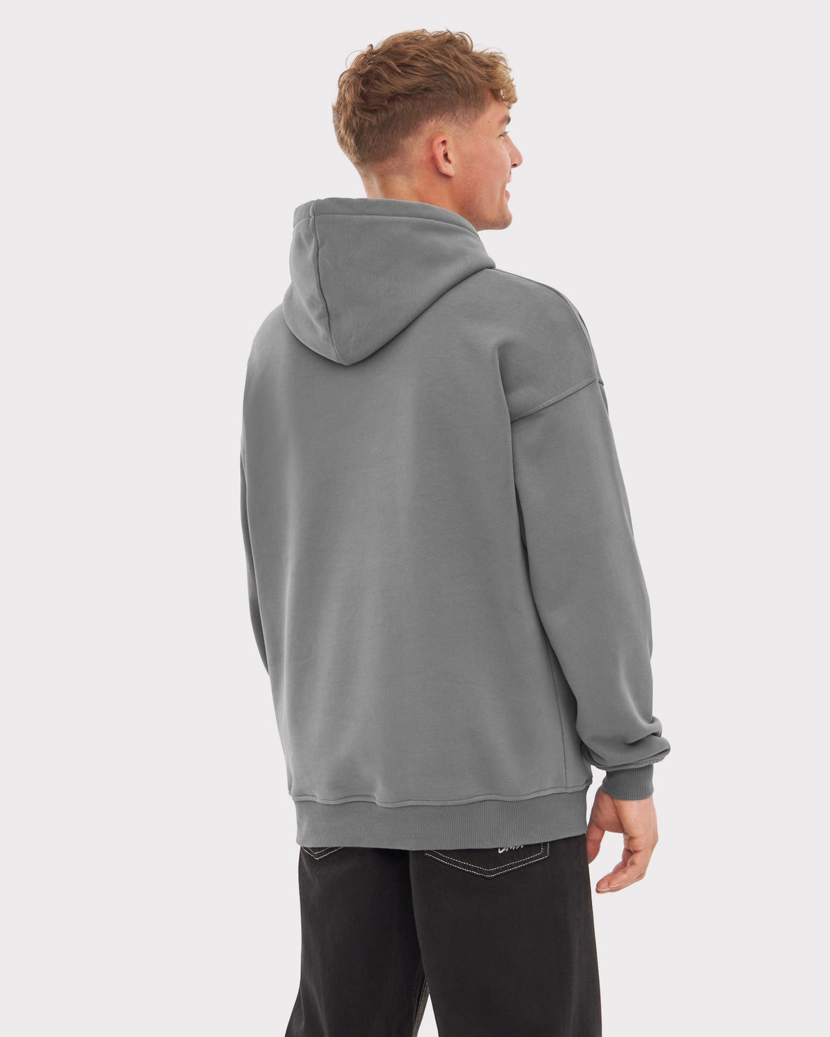 Mann von hinten in grauem oversized Hoodie 'Cody' mit Kapuze, trägt schwarze Jeans