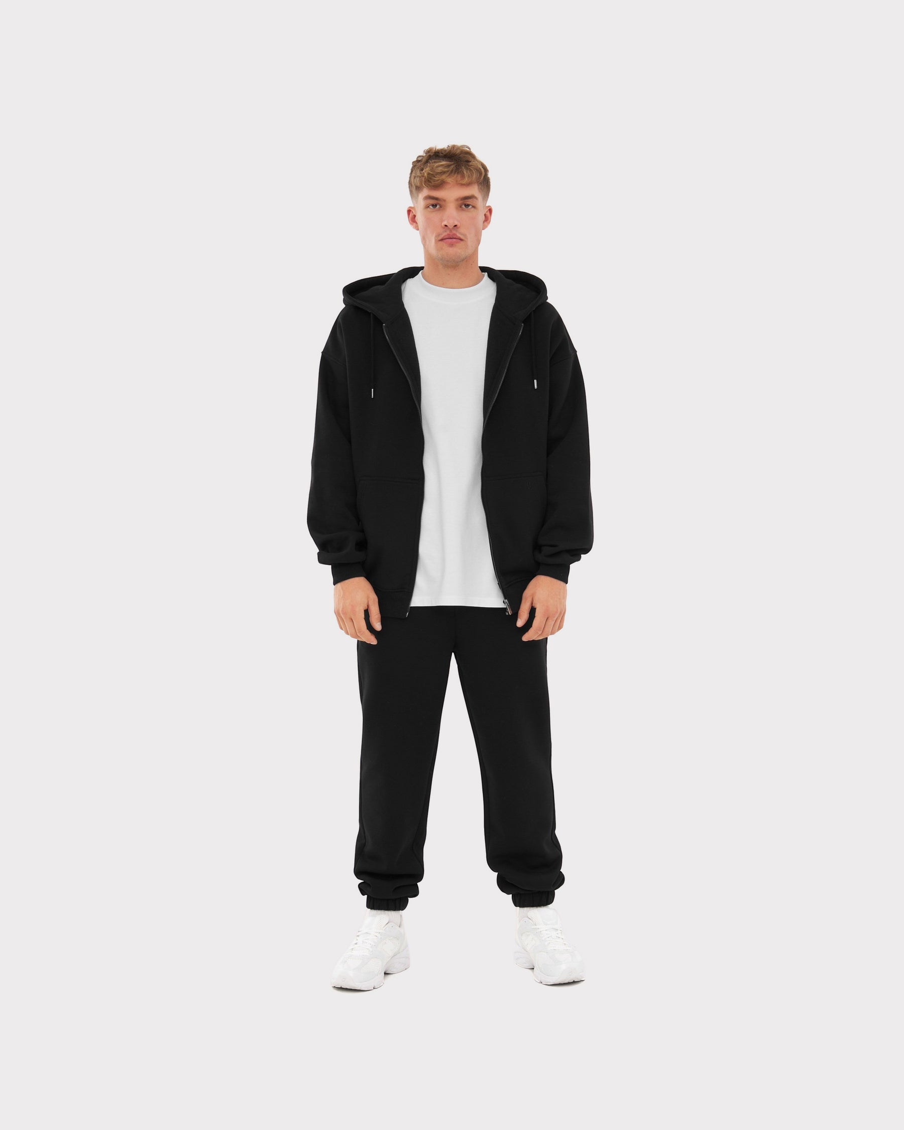 Mann trägt schwarze Jogginghose 'Owen' von Johnny Urban mit weißem T-Shirt, schwarzer Zip-Hoodie und weißen Sneakern