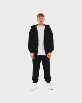 Mann trägt schwarze Jogginghose 'Owen' von Johnny Urban mit weißem T-Shirt, schwarzer Zip-Hoodie und weißen Sneakern