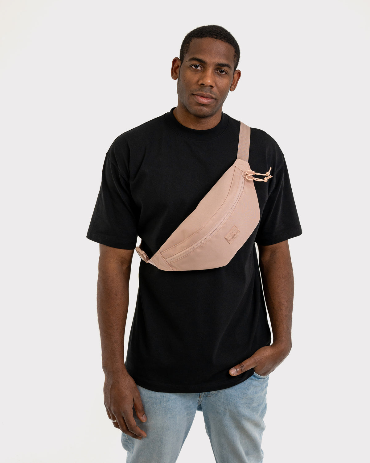 Mann trägt Bauchtasche 'Erik Large' in Rosa quer über der Brust, kombiniert mit schwarzem T-Shirt und blauer Jeans