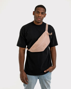 Mann trägt Bauchtasche 'Erik Large' in Rosa quer über der Brust, kombiniert mit schwarzem T-Shirt und blauer Jeans