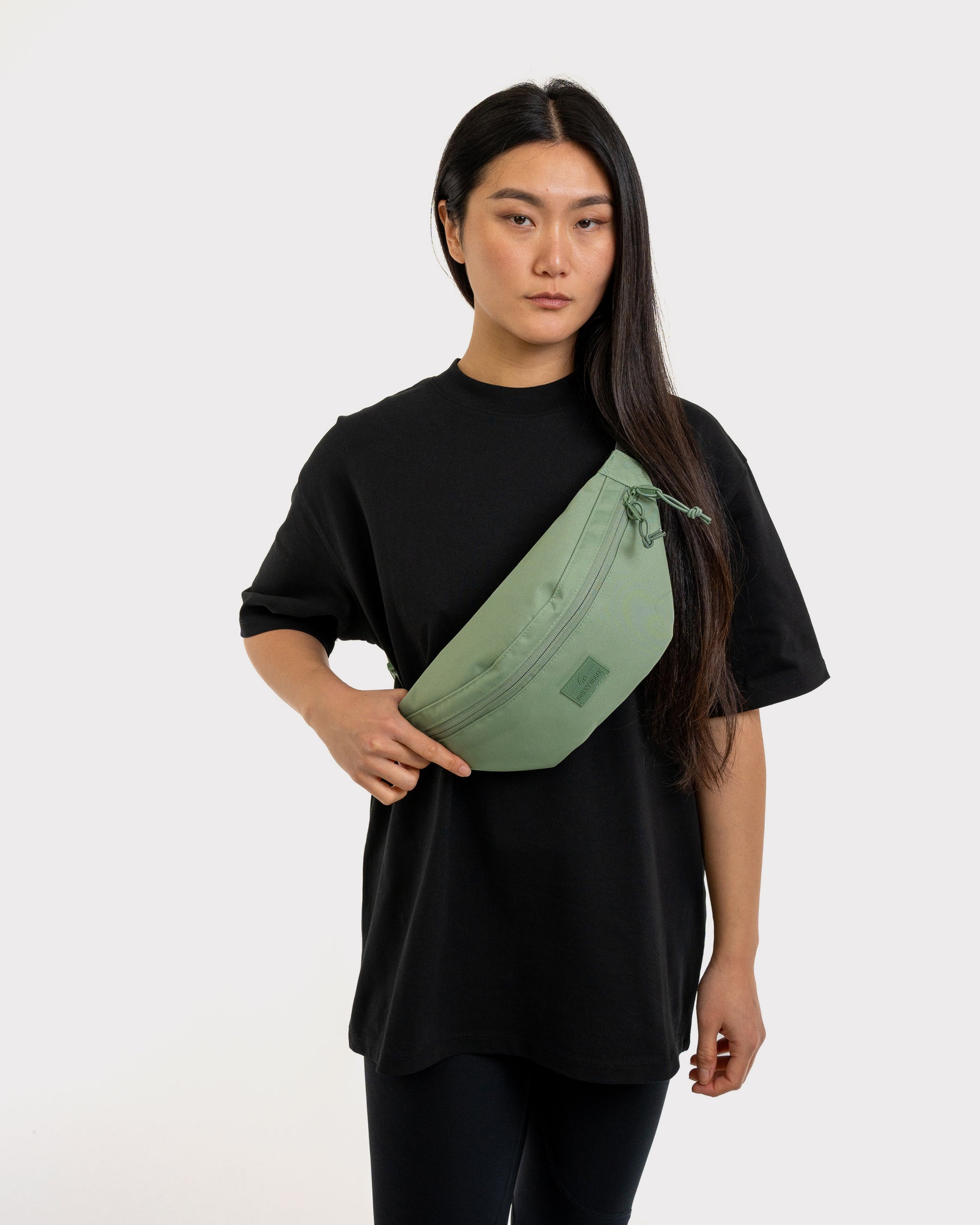 Frau trägt sage-green Bauchtasche 'Erik Large' von Johnny Urban über der Schulter mit schwarzem Shirt