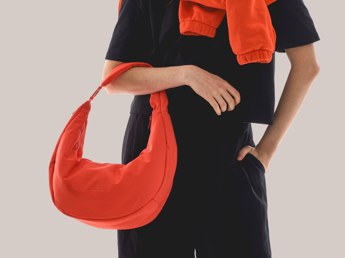 Unser weibliches Model präsentiert hier die Half-Moon-Bag "Cleo" in coral-rot. 