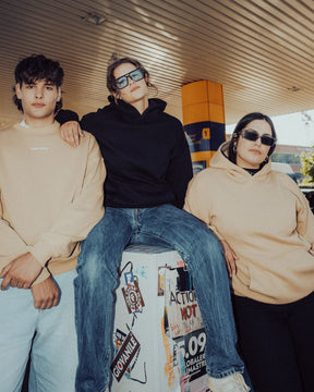 Drei junge Menschen tragen oversized Hoodies 'Cody', zwei in Beige und einer in Schwarz, in urbaner Umgebung