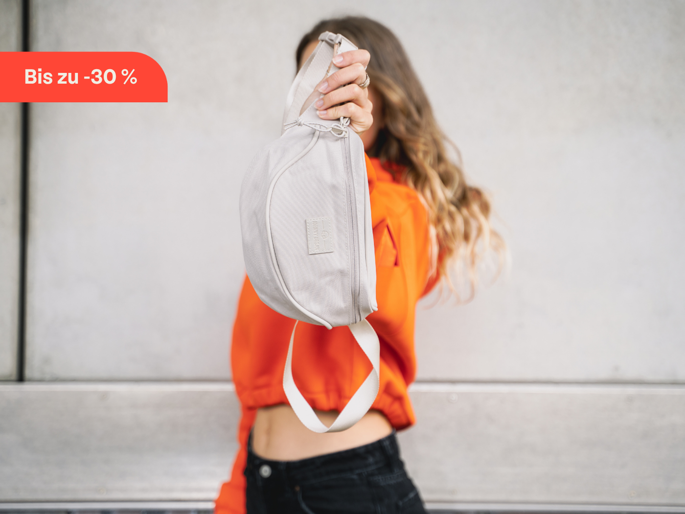 Frau hält Bauchtasche "Ben" in creme in die Kamera.