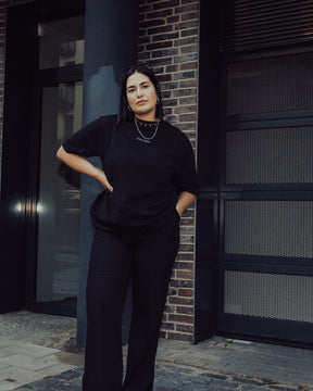 Frau trägt schwarz oversized T-Shirt 'Sammy Johnny Urban' und schwarze Hose vor urbanem Hintergrund