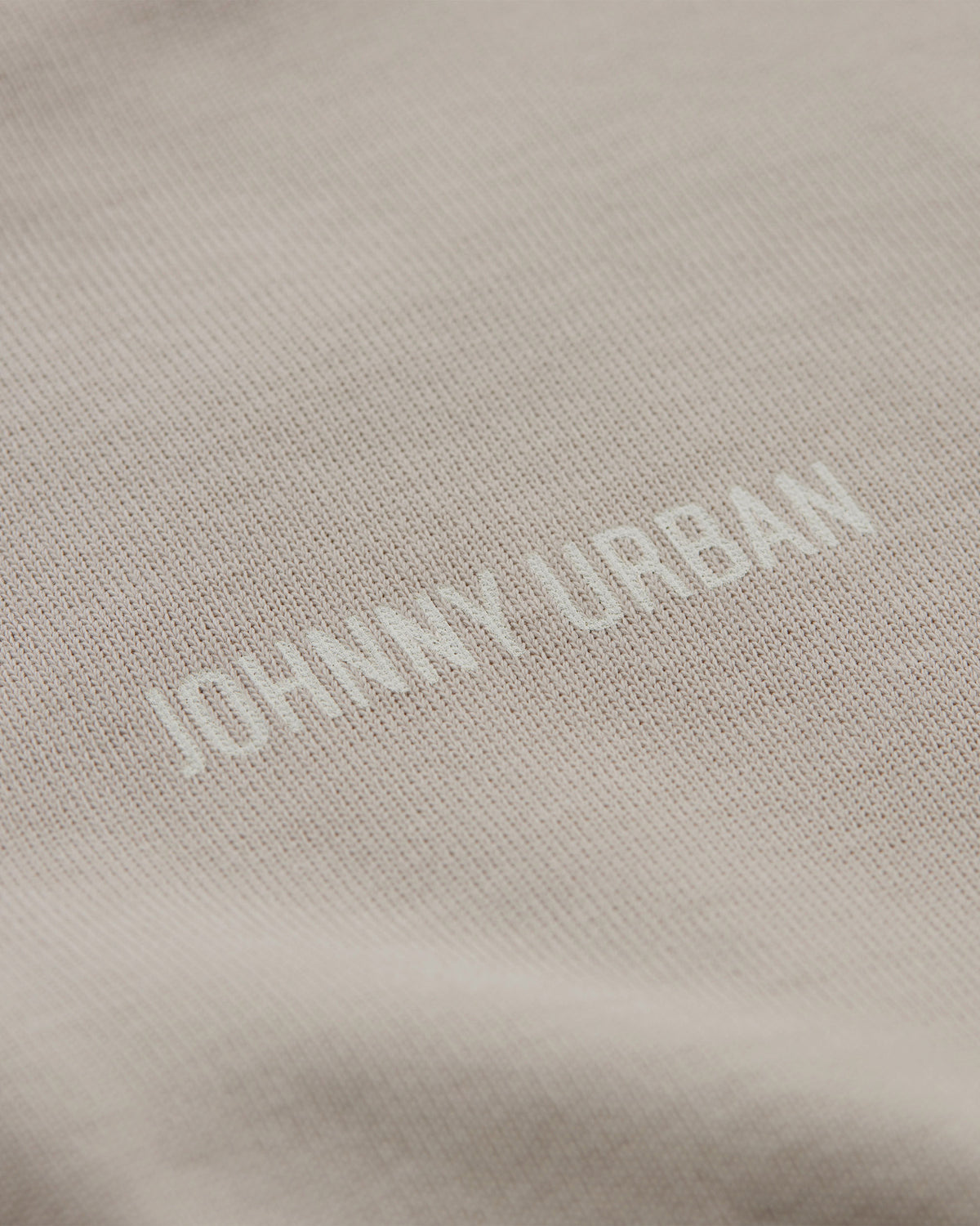Detailaufnahme eines beigen T-Shirts mit geprägtem 'Johnny Urban' Schriftzug