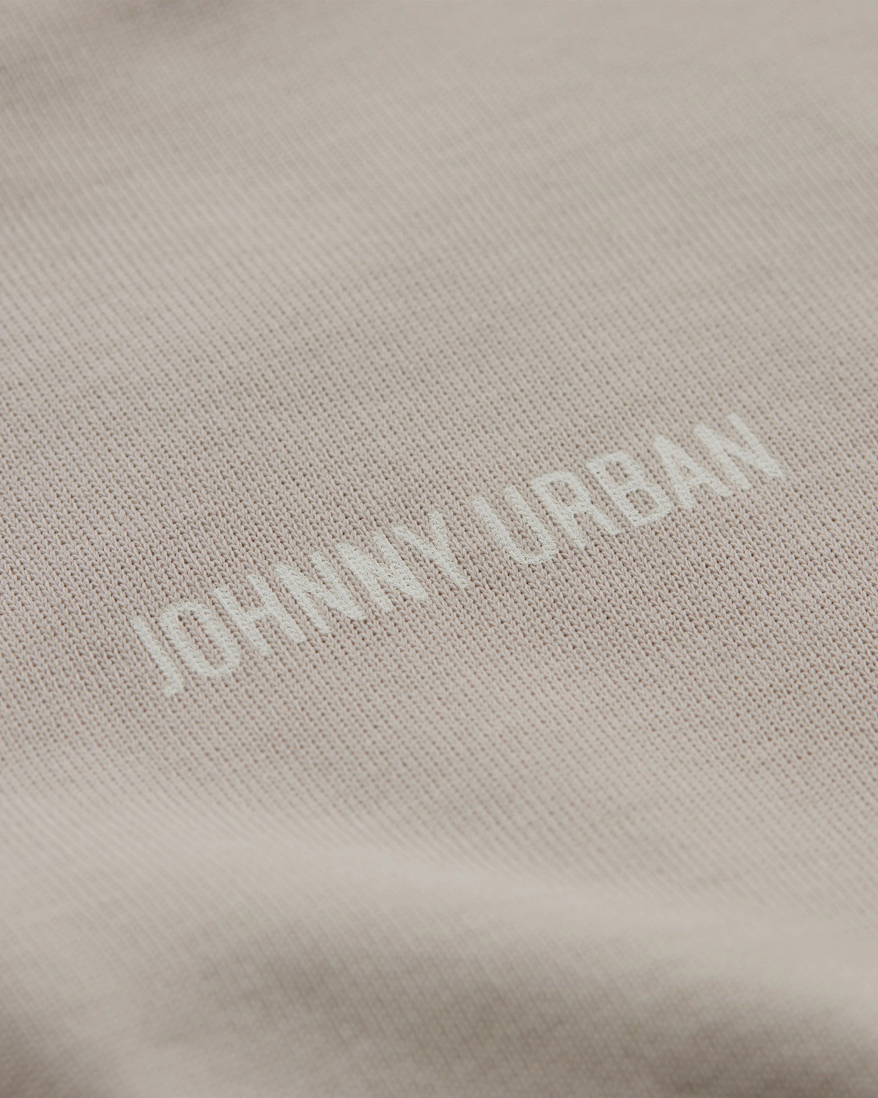 Detailaufnahme eines beigen T-Shirts mit geprägtem 'Johnny Urban' Schriftzug