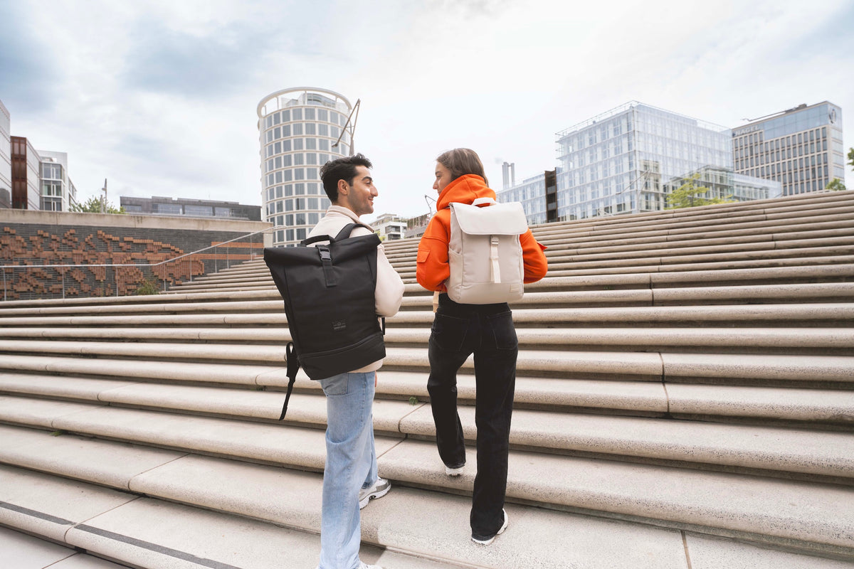 Ein Mann und eine Frau laufen mit Johnny Urban Rolltop Rucksäcken die Treppen hinauf. 