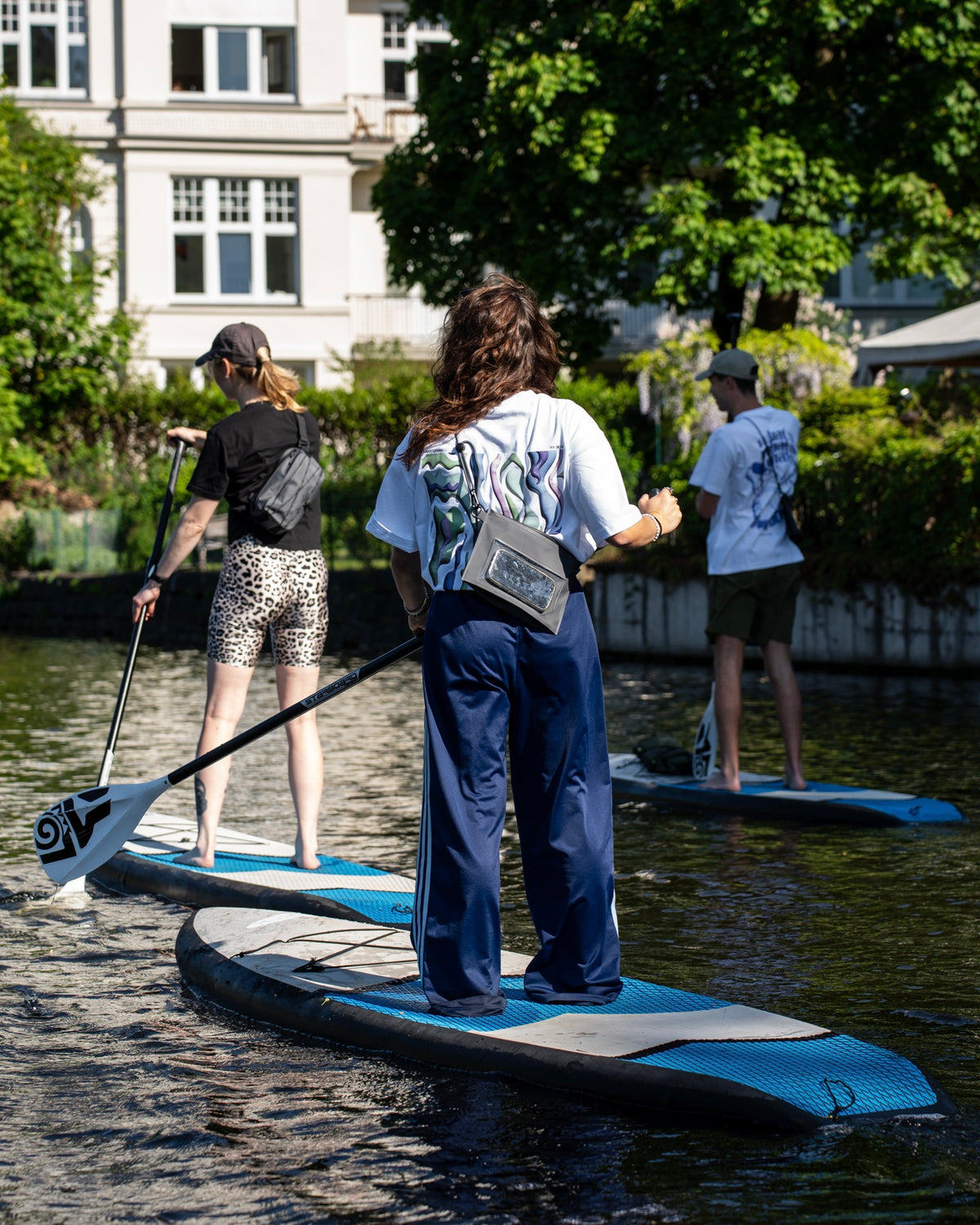 Frau steht auf einen Sup mit einem Paddel in der Hand und trägt eine wasserfeste Tasche.