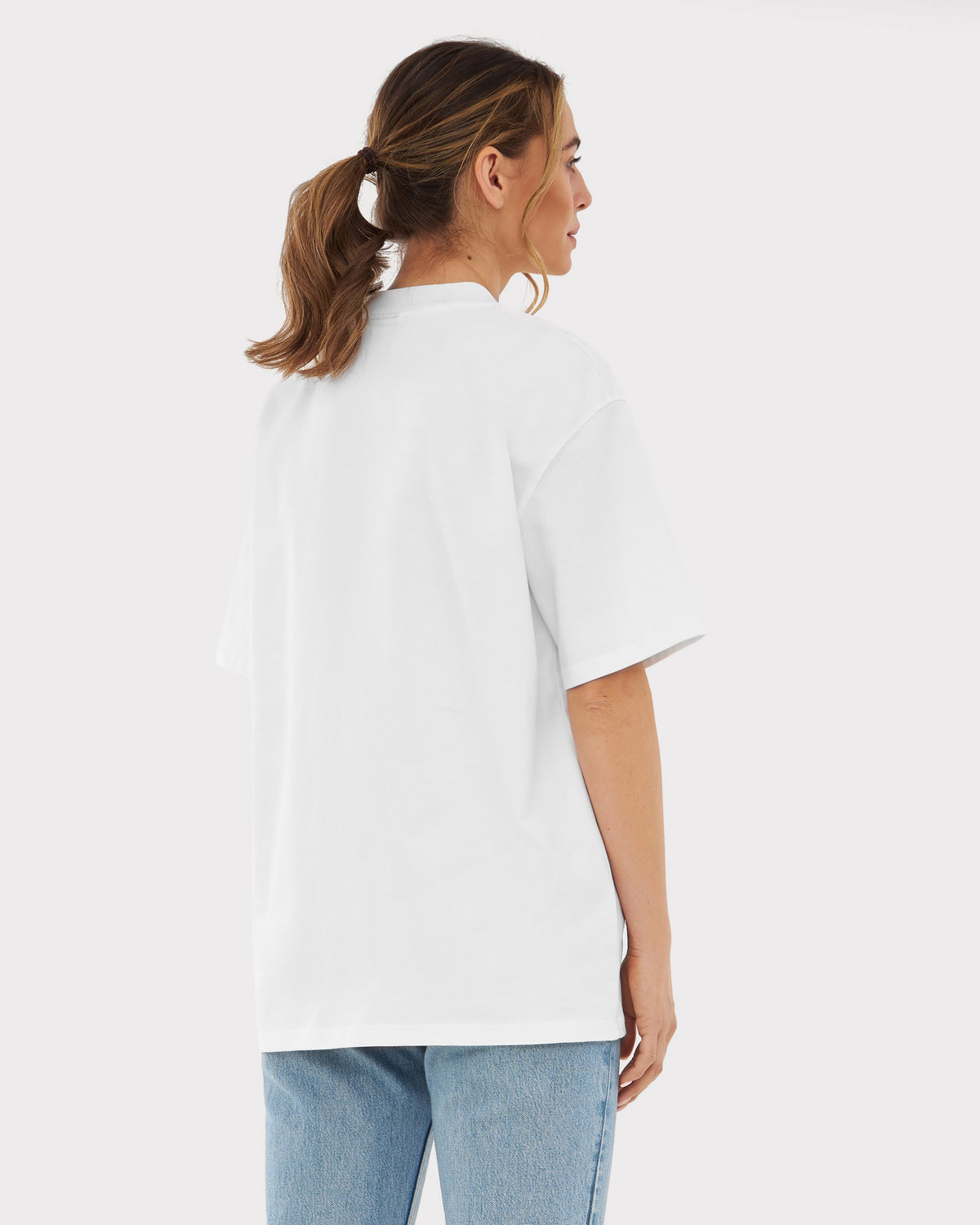 Frau trägt oversized T-Shirt 'Sammy' in Weiß, Rückansicht, mit blonden Zöpfen, dazu blaue Jeans
