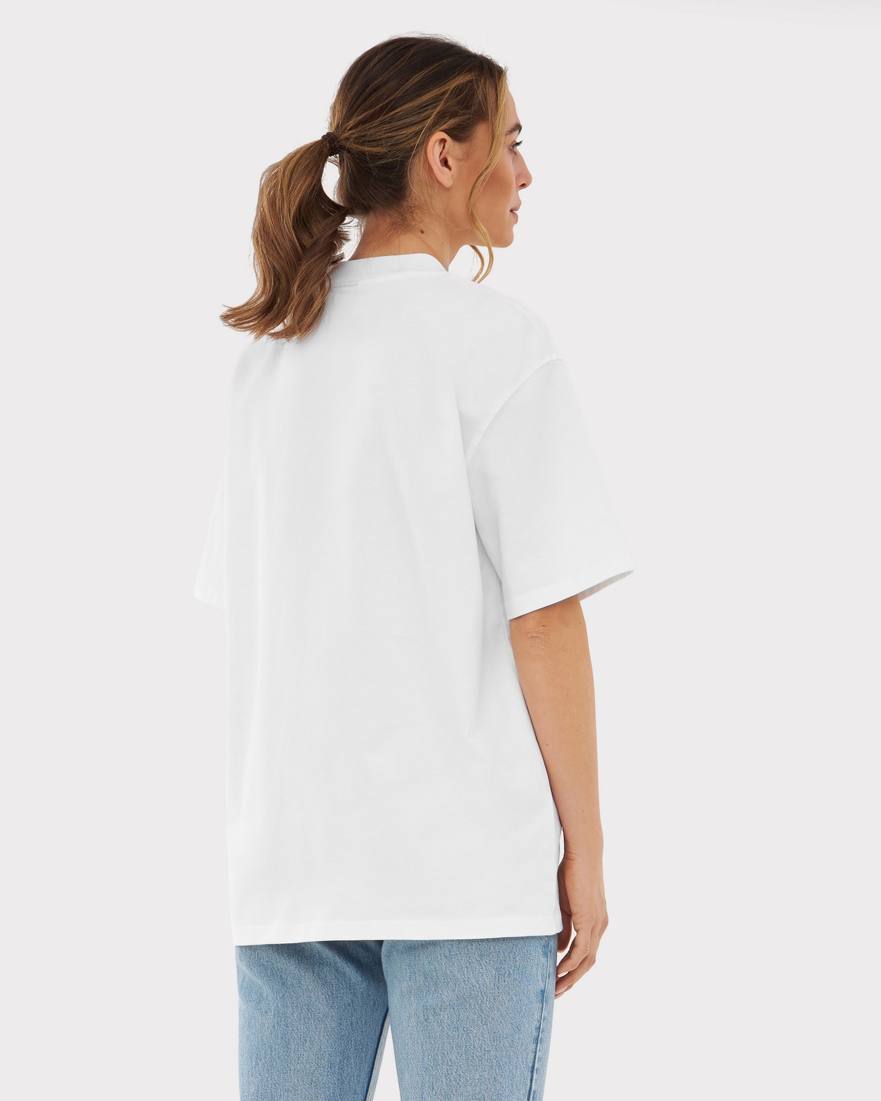 Frau trägt oversized T-Shirt 'Sammy' in Weiß, Rückansicht, mit blonden Zöpfen, dazu blaue Jeans