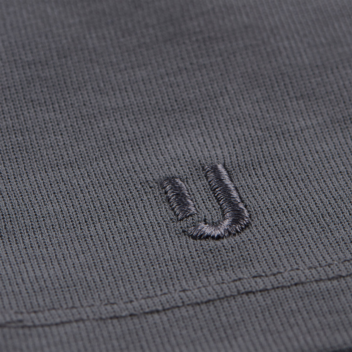 Nahaufnahme des grauen Baumwollstoffs eines T-Shirts mit eingesticktem 'ju'-Logo