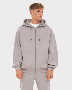 Mann trägt oversized Zip Hoodie 'Caleb' in Grau mit Kapuze, Reißverschluss und Kängurutaschen.
