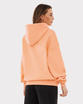 Rückansicht eines Modells mit oversized Kapuzenpullover 'Cody' in Pfirsich und schwarzer Hose