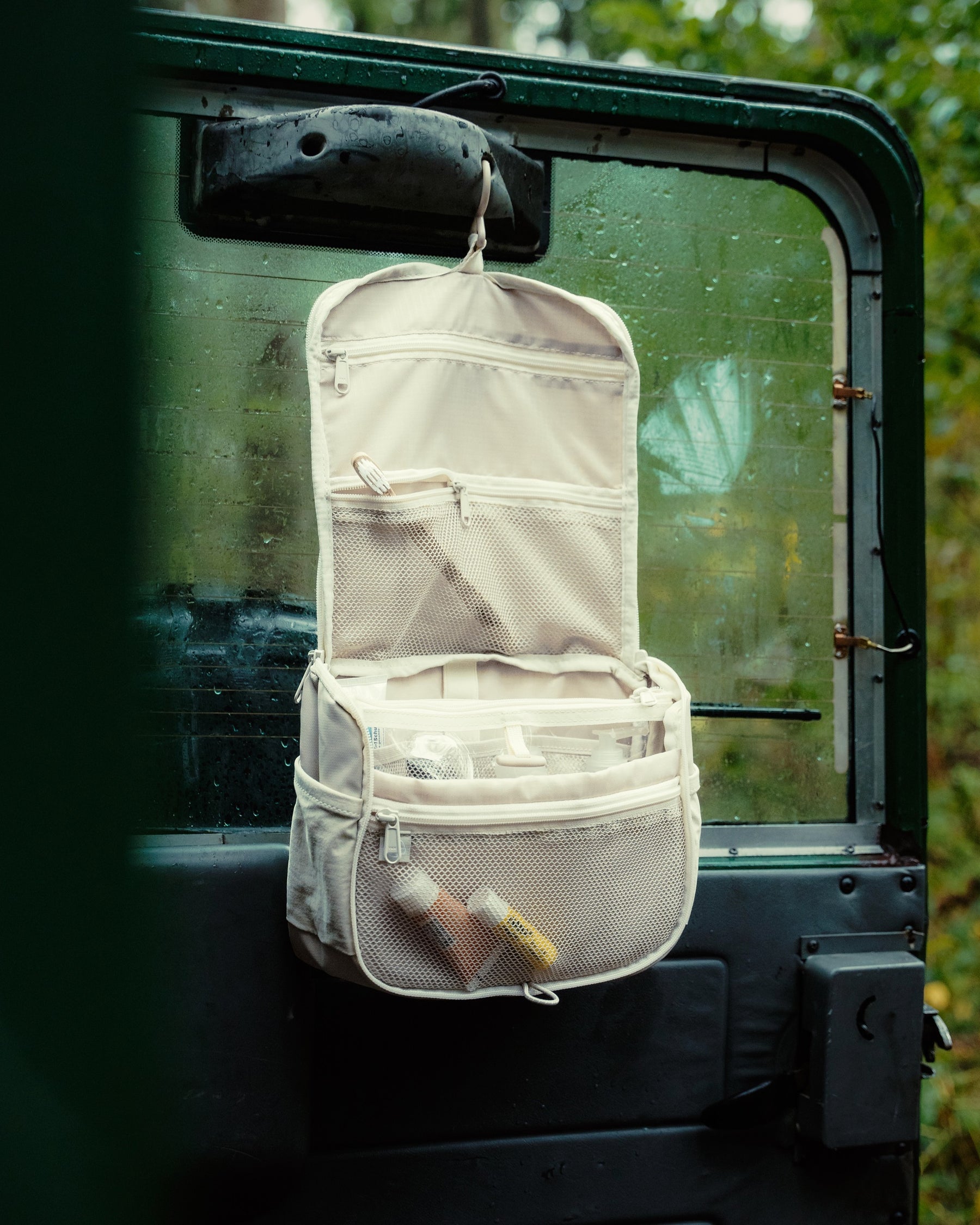 Beige Kulturtasche 'Logan' von Johnny Urban mit mehreren Taschen hängt an einer Autotür