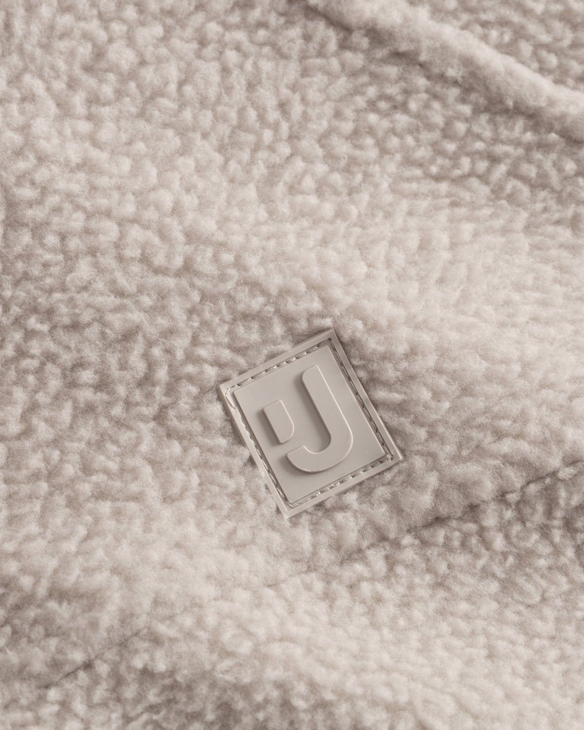 Unser hochwertiges Logo-Badge auf der Fleecejacke Nova in Beige.  
