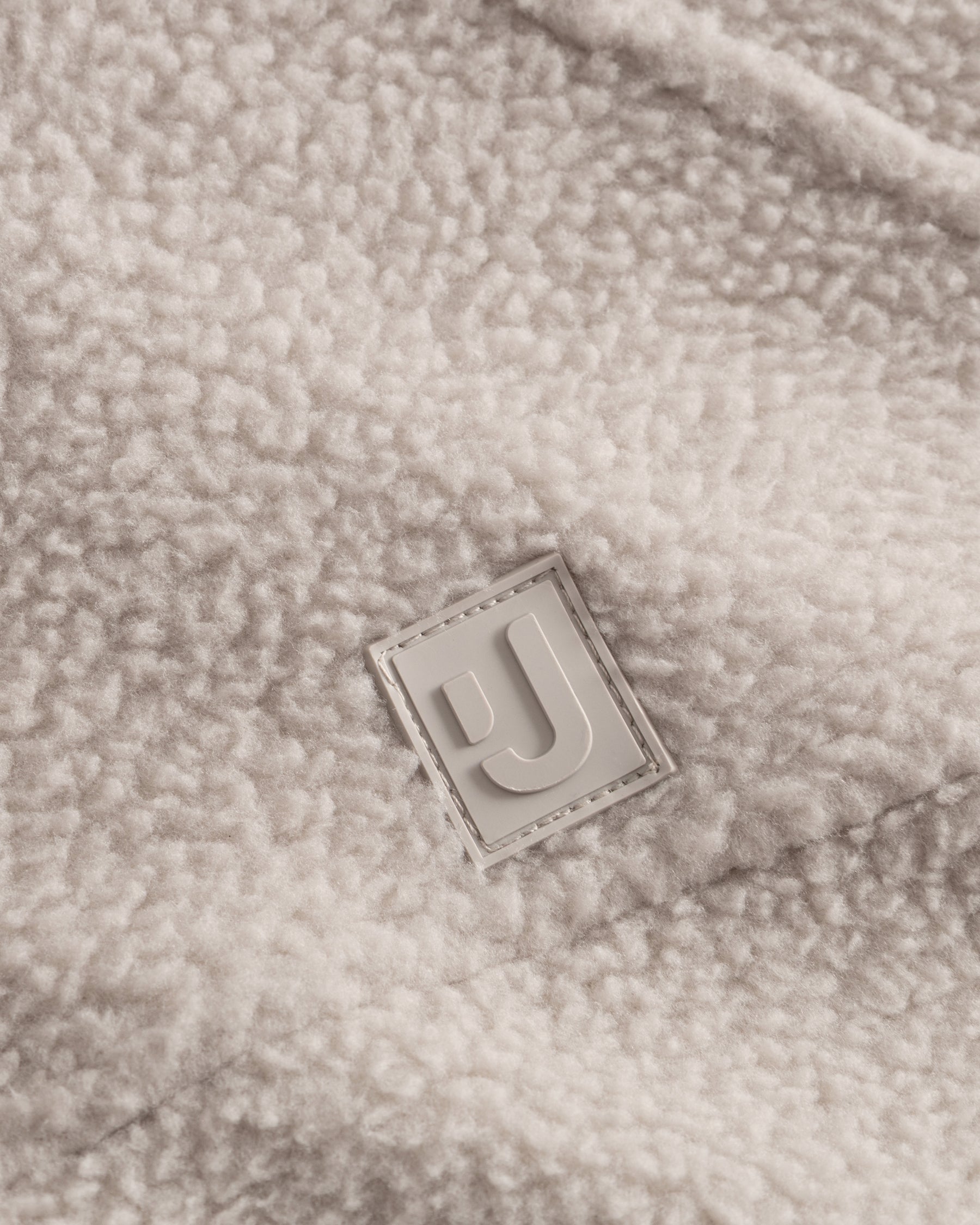 Unser hochwertiges Logo-Badge auf der Fleecejacke Nova in Beige.  
