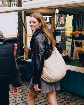 Frau trägt beige Half Moon Bag 'Kaia XL' von Johnny Urban, neben ihr Mann mit großem schwarzem Rucksack, Marktstand im Hintergrund