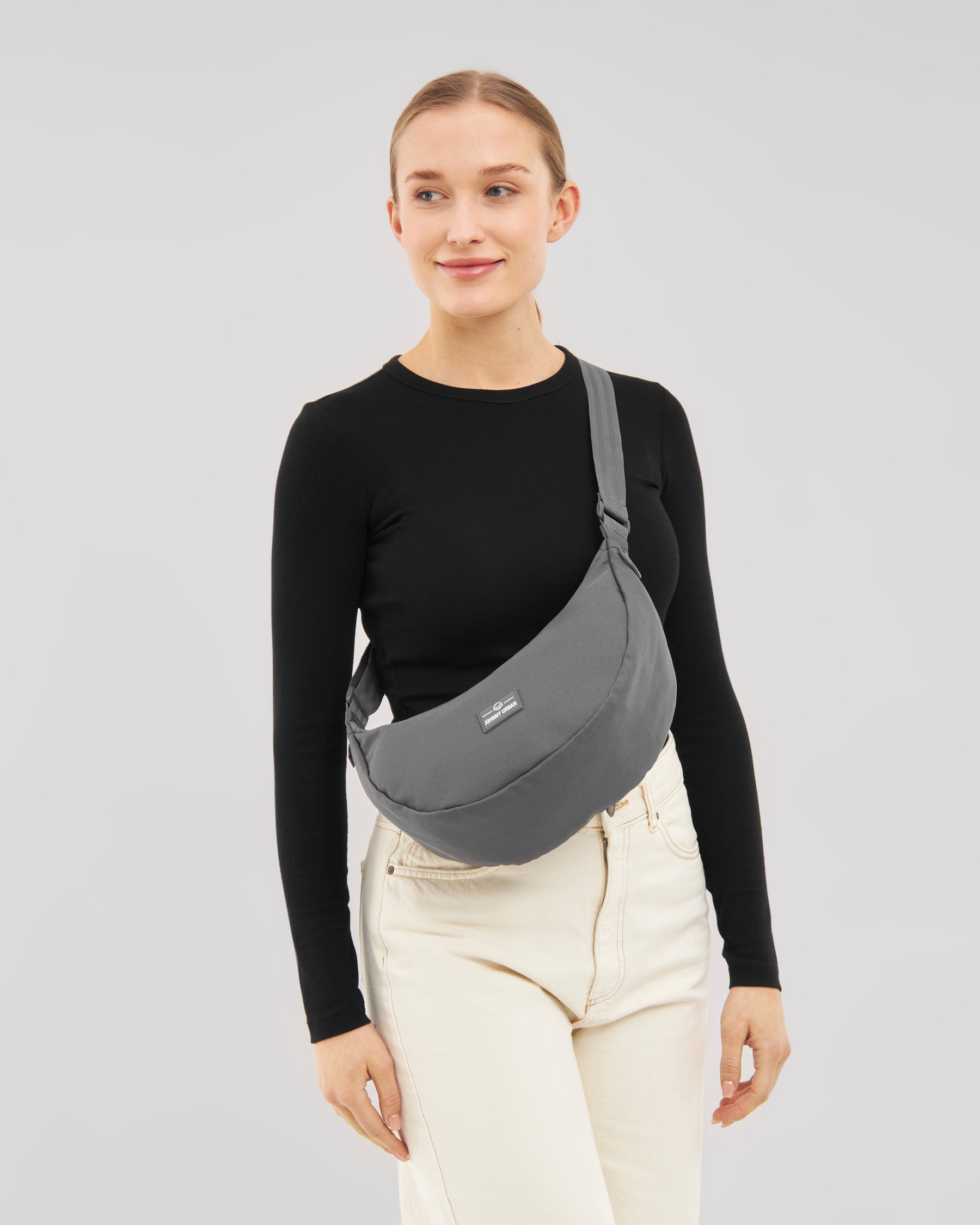 Frau mit schwarzem Langarmshirt und hellen Hosen trägt halbrunde, graue Half Moon Bag 'Ally Medium' quer über dem Oberkörper