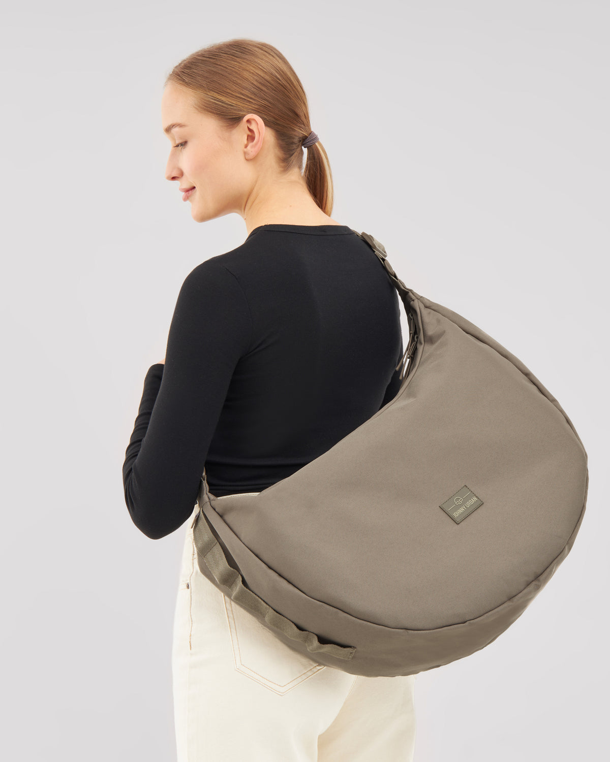 Frau mit schwarzem Oberteil trägt die halbmondförmige Half Moon Bag 'Ally XL' in graubraun über der Schulter