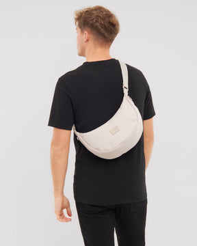 Mann mit schwarzem T-Shirt trägt die halbrunde Tasche 'Ally Medium' in hellem Farbton über der Schulter