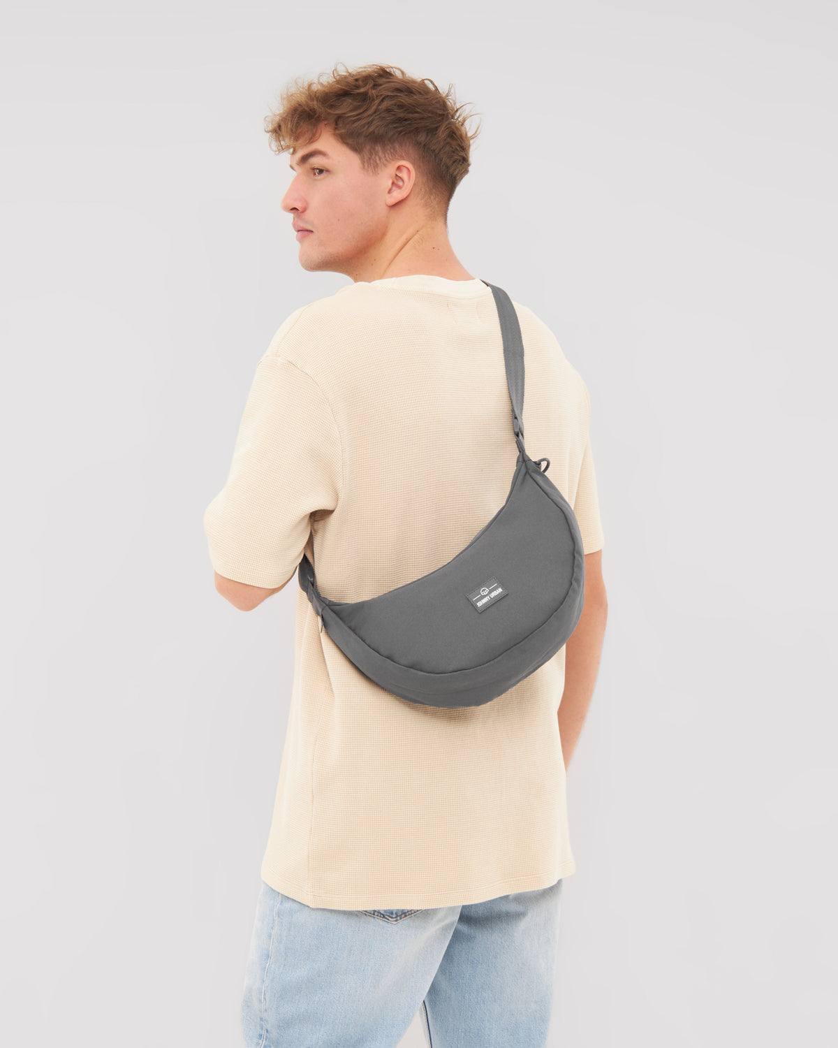 Mann trägt die halbmondförmige Tasche 'Ally Medium' von Johnny Urban in Grau über der Schulter