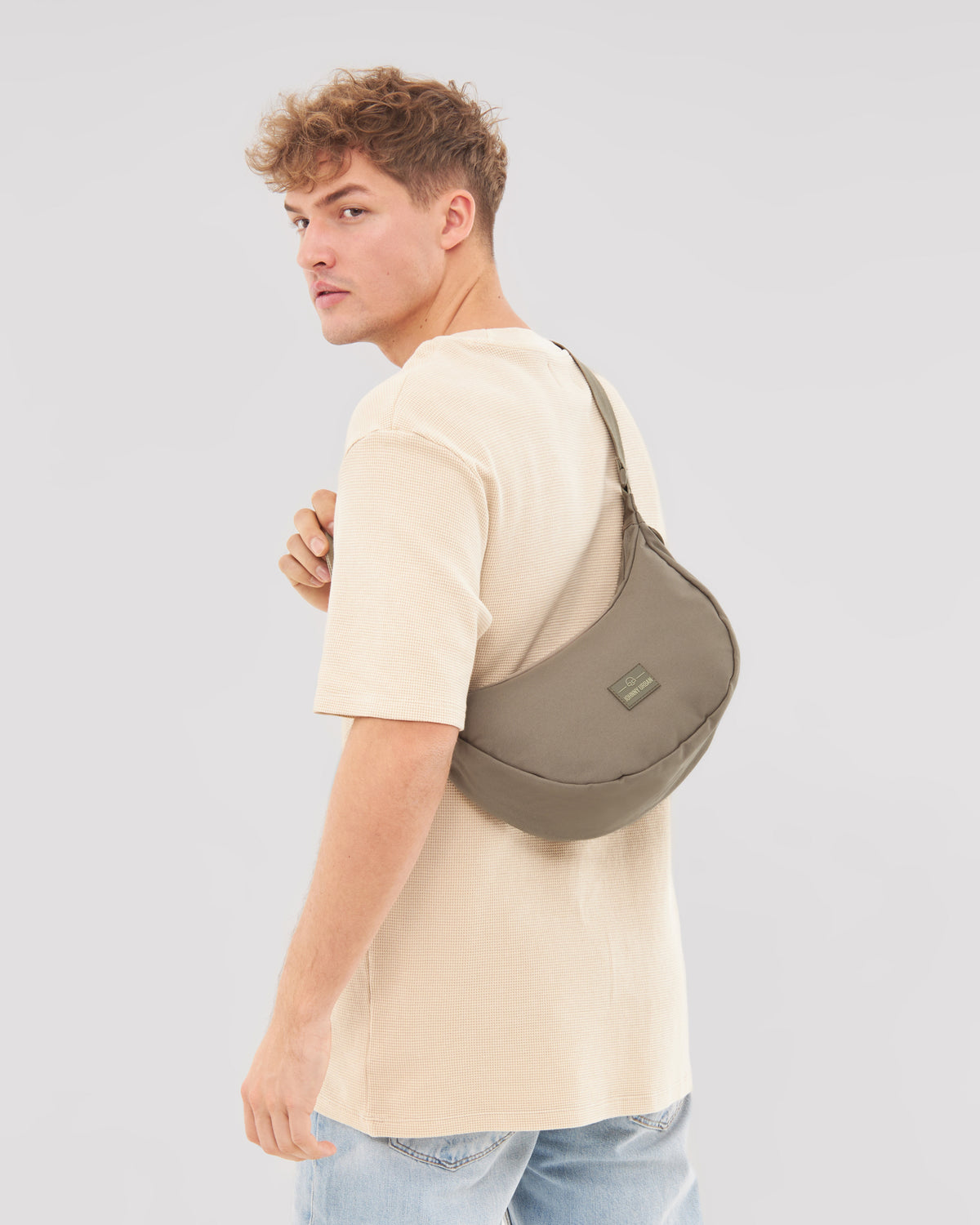 Mann trägt die Half Moon Bag 'Ally Medium' von Johnny Urban in taupe über der Schulter