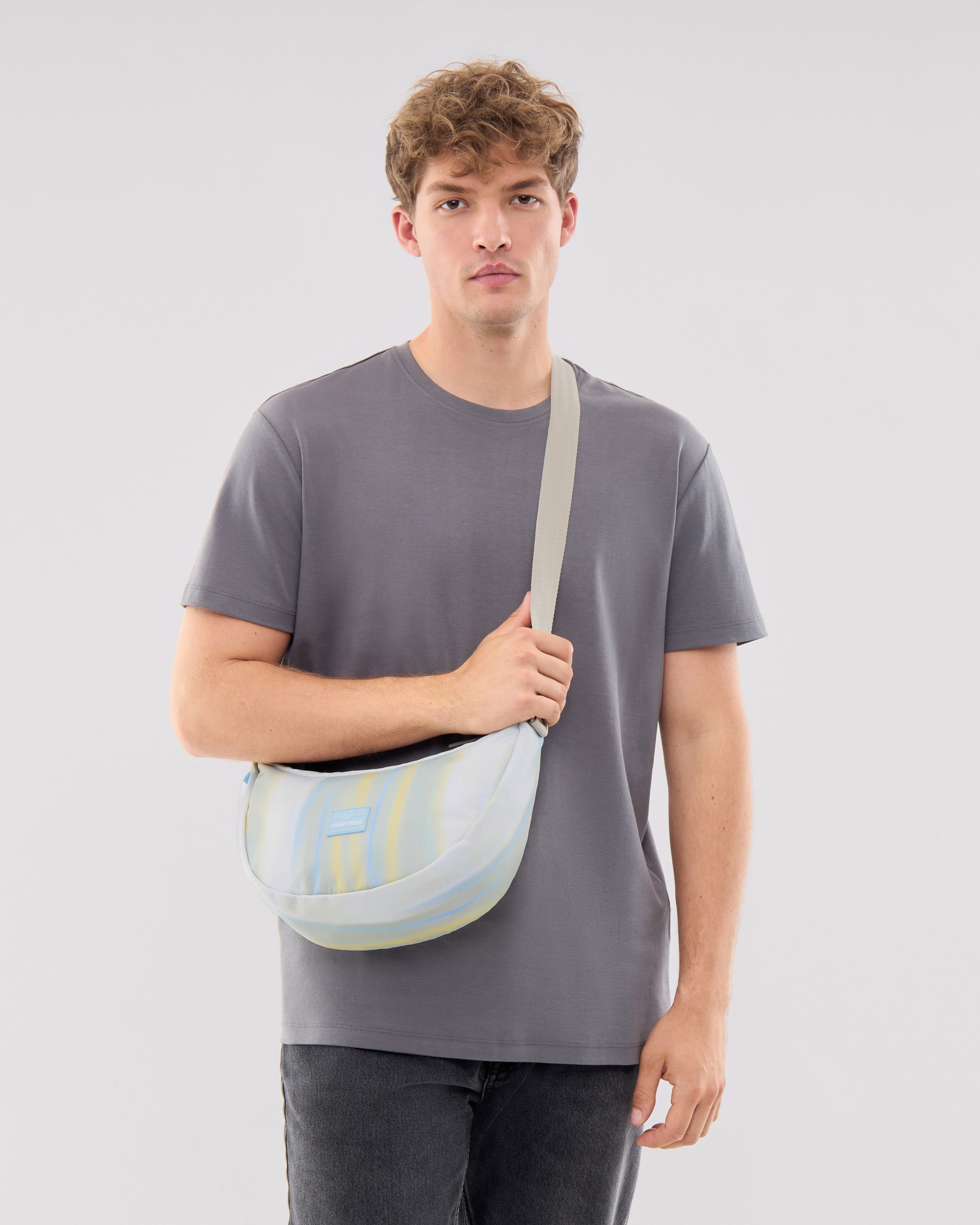 Mann trägt Half Moon Bag 'Ally Medium' quer über der Schulter, farblich gestreift in Pastelltönen