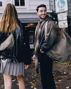 Mann und Frau tragen halbmondförmige Johnny Urban 'Ally XL' Taschen in Olivegrün in einer städtischen Umgebung