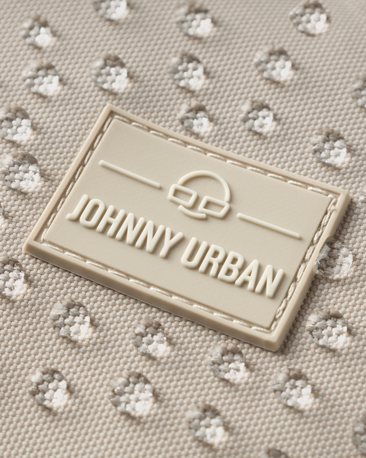 Nahaufnahme des Johnny Urban Logos auf wasserabweisendem hellbeigem Stoff mit Wassertropfen