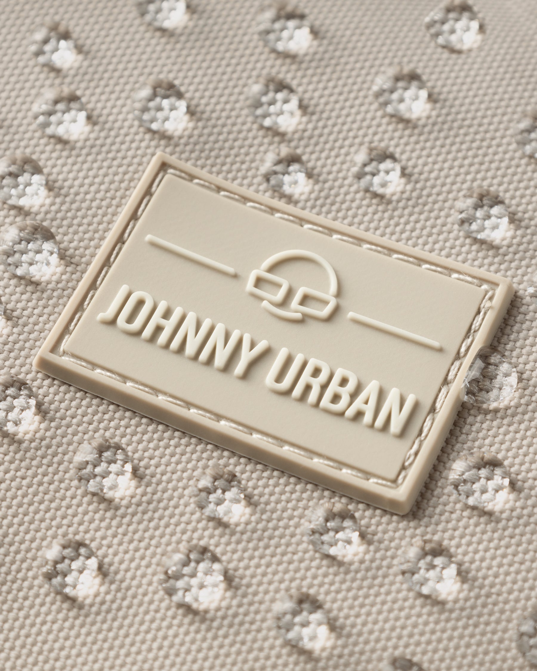 Nahaufnahme des Johnny Urban Logos auf wasserabweisendem hellbeigem Stoff mit Wassertropfen