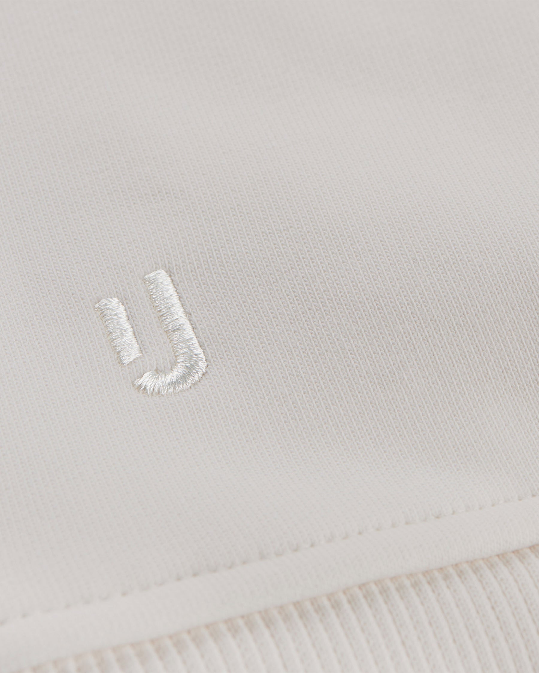 Nahaufnahme des cremefarbenen Oversized Crewnecks 'Carter' von Johnny Urban mit weißem gesticktem Logo