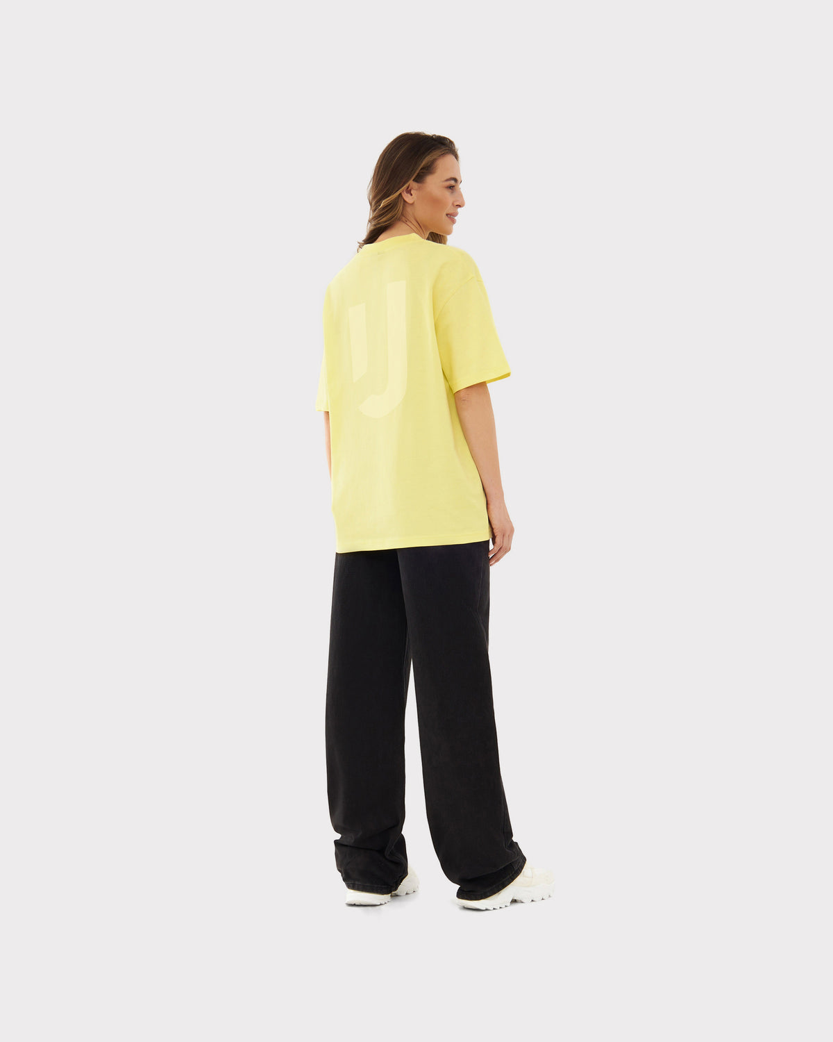 Frau trägt oversized gelbes T-Shirt 'Sammy JU' von Johnny Urban, schwarze Hose, weiße Schuhe, Rückenansicht