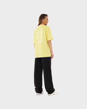 Frau trägt oversized gelbes T-Shirt 'Sammy JU' von Johnny Urban, schwarze Hose, weiße Schuhe, Rückenansicht