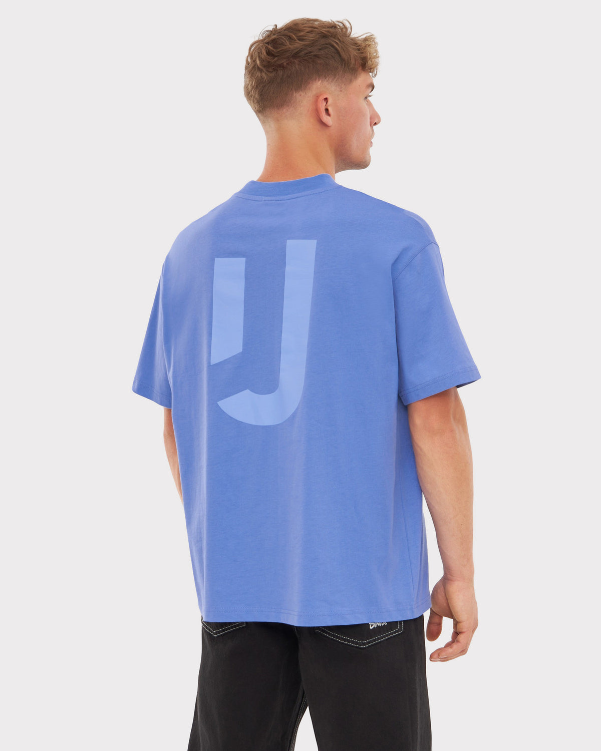 Mann trägt oversized blau-lila T-Shirt 'Sammy JU' mit großem 'JU'-Print auf dem Rücken