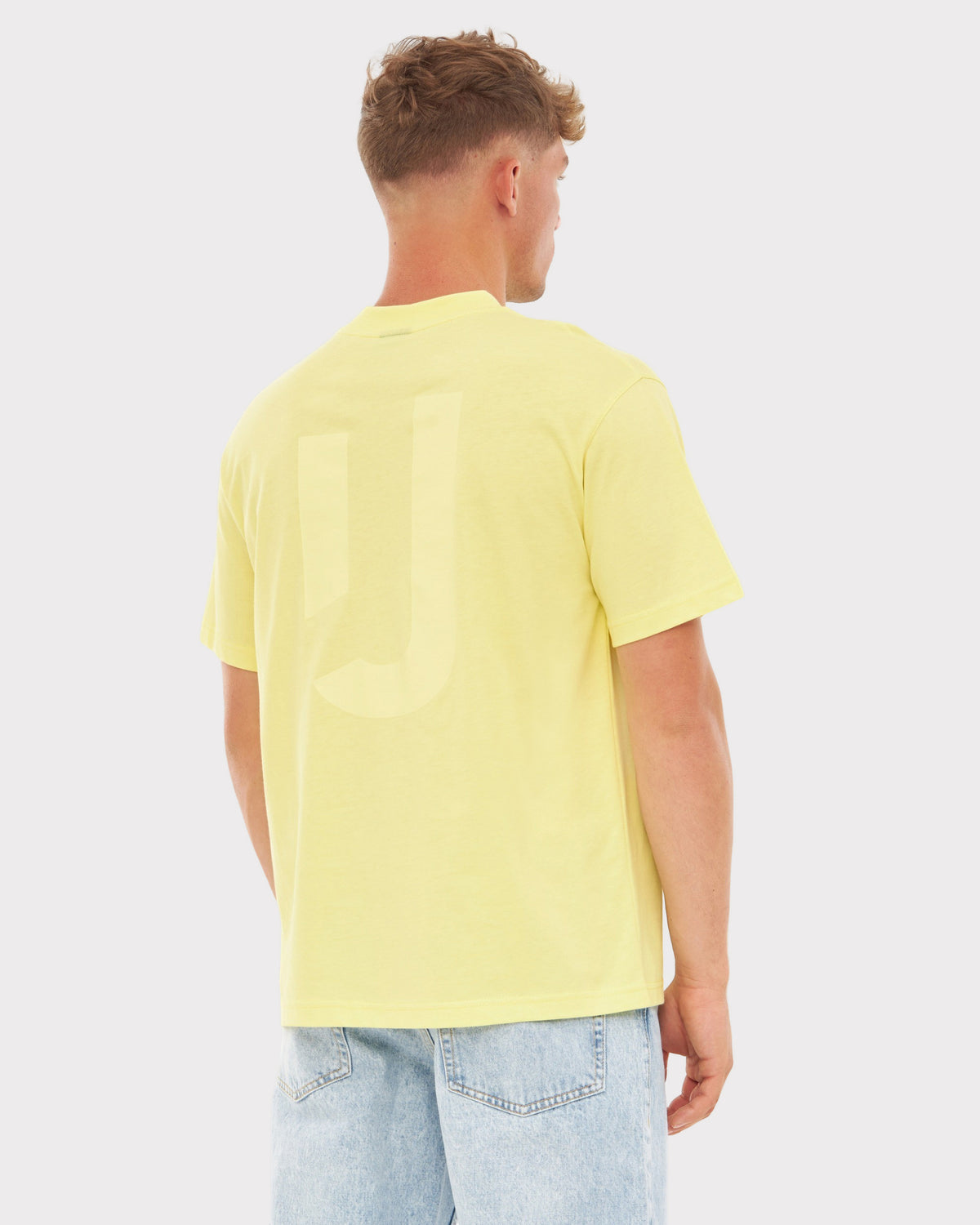 Mann trägt gelbes Oversize-T-Shirt 'Sammy JU' mit dezentem 'JU'-Print auf dem Rücken