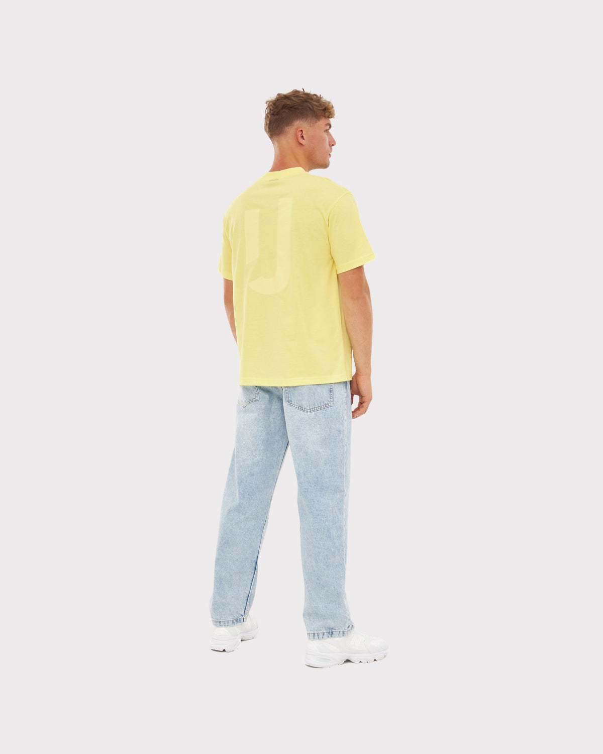 Mann von hinten mit gelbem Oversize-T-Shirt ‚Sammy JU‘ von Johnny Urban, hellblaue Jeans und weißen Schuhen