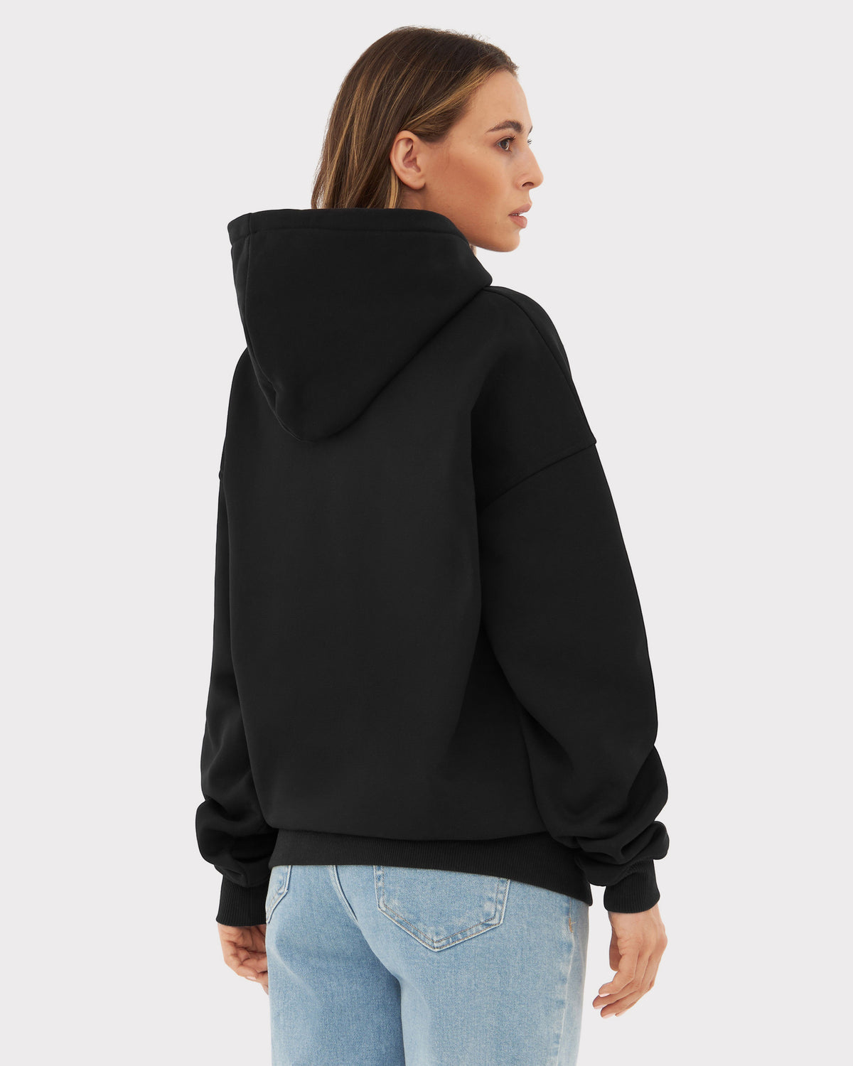 Rückansicht einer Frau mit schwarzem übergroßen Hoodie 'Cody' von Johnny Urban und hellblauen Jeans