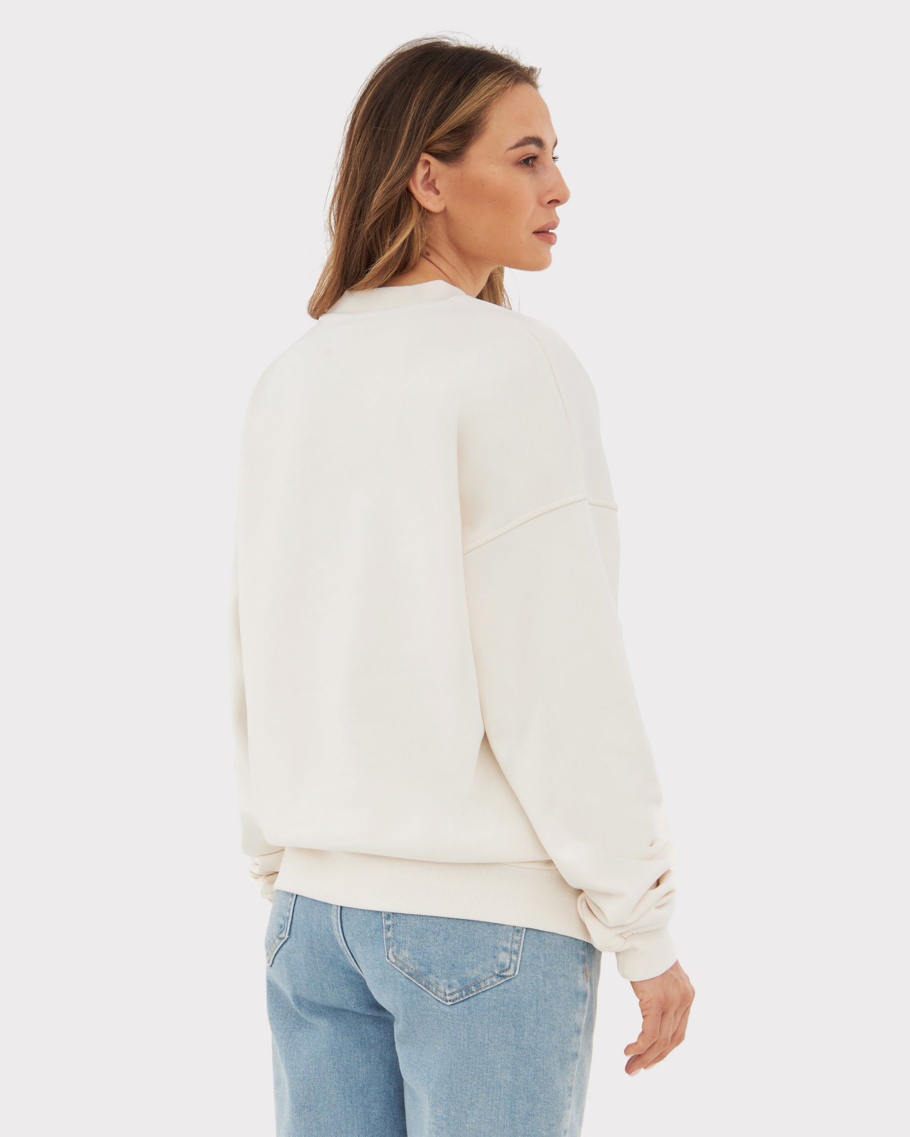 Frau trägt weißen oversized Crewneck-Sweatshirt 'Carter' von hinten mit blauen Jeans