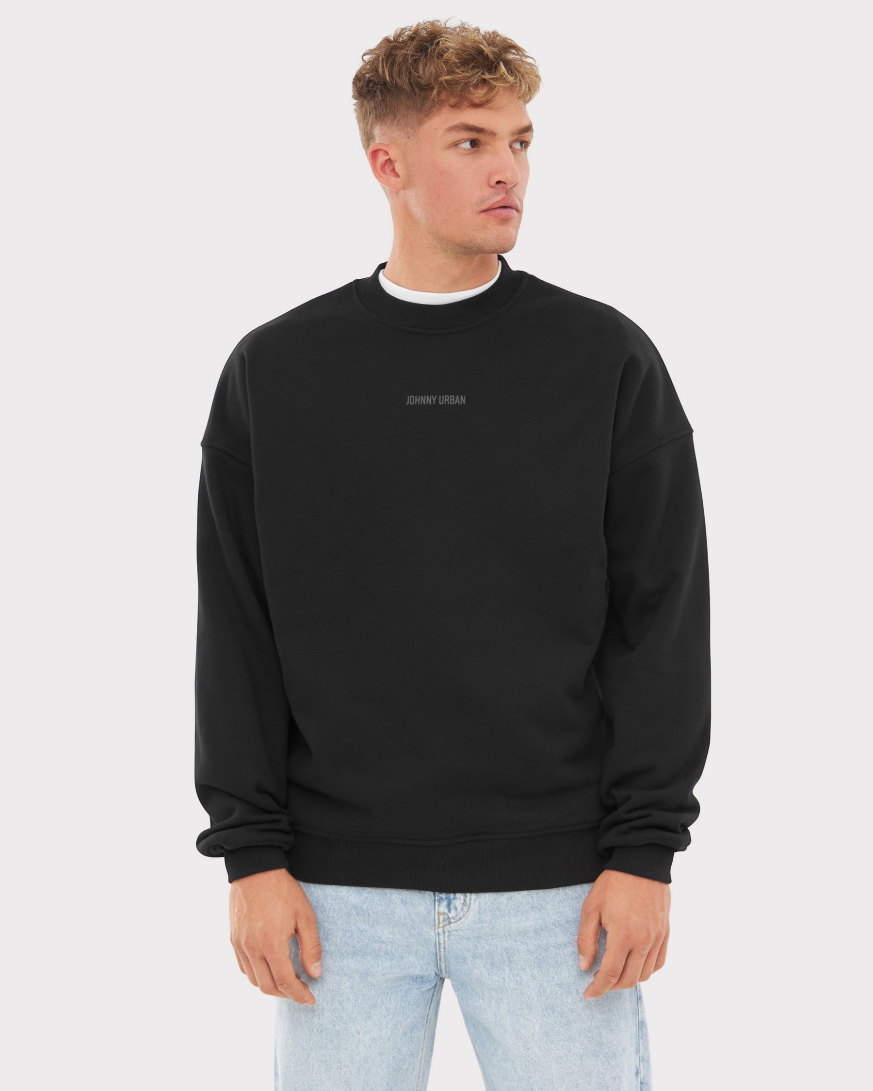 Mann trägt schwarzen oversized Crewneck 'Carter' mit kleinem Johnny Urban Print auf der Brust