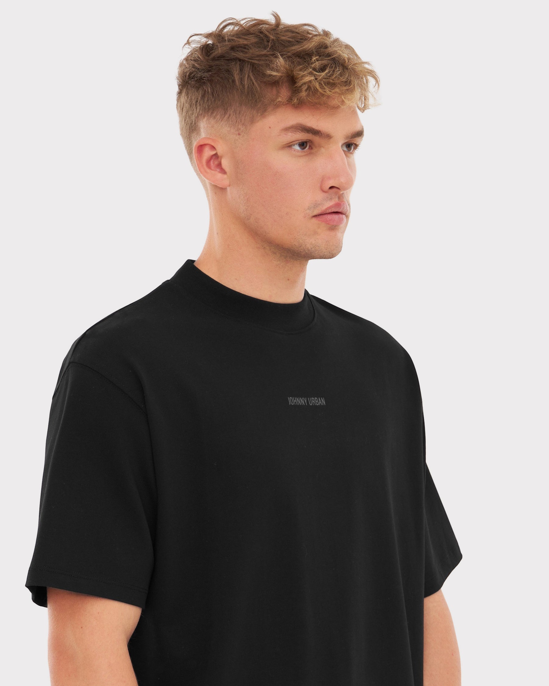 Mann trägt oversized schwarzes T-Shirt 'Sammy Johnny Urban' mit kleinem Schriftzug vorne