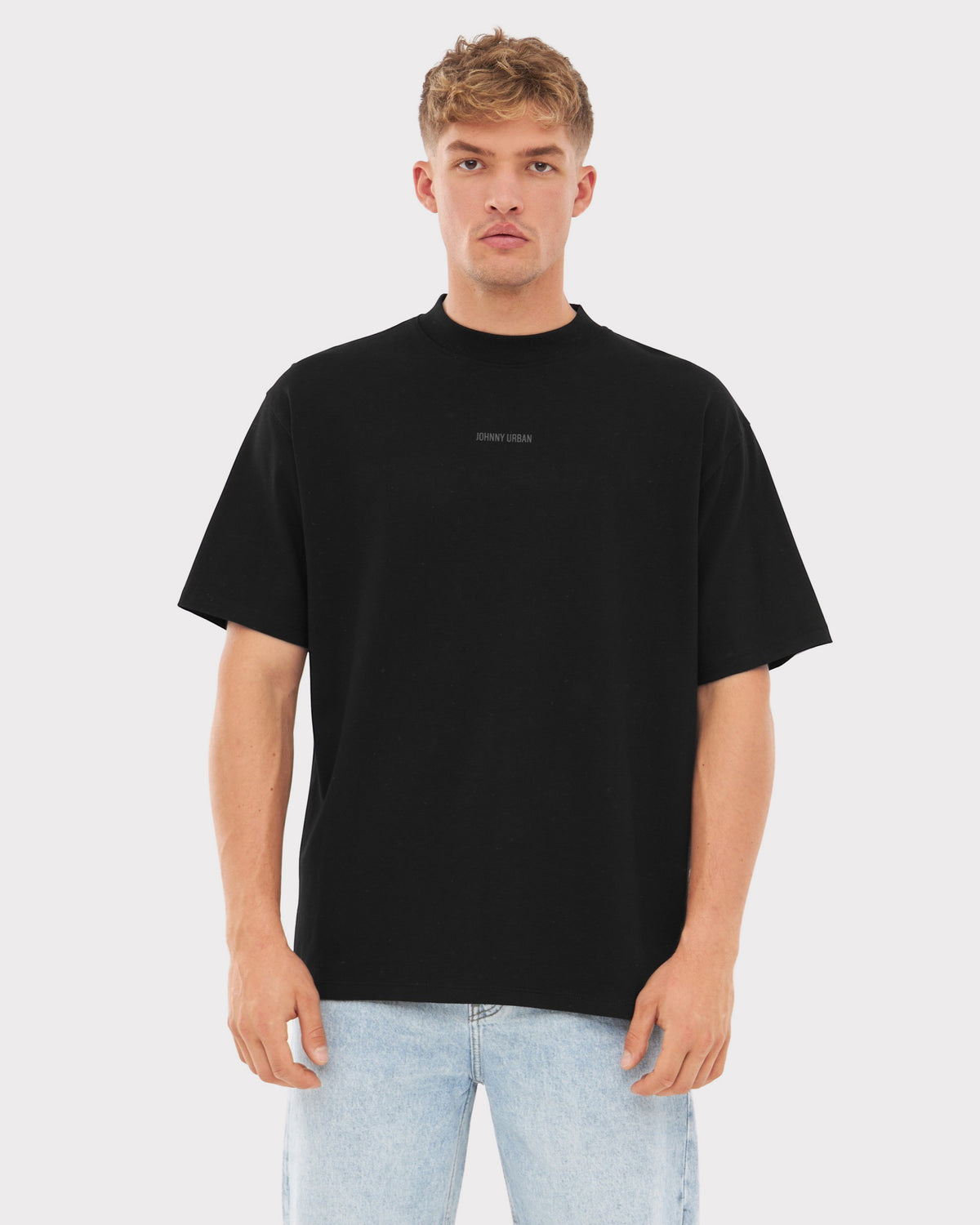 Mann trägt schwarzes Oversized-T-Shirt 'Sammy Johnny Urban' mit kleinem Aufdruck, helle Jeans