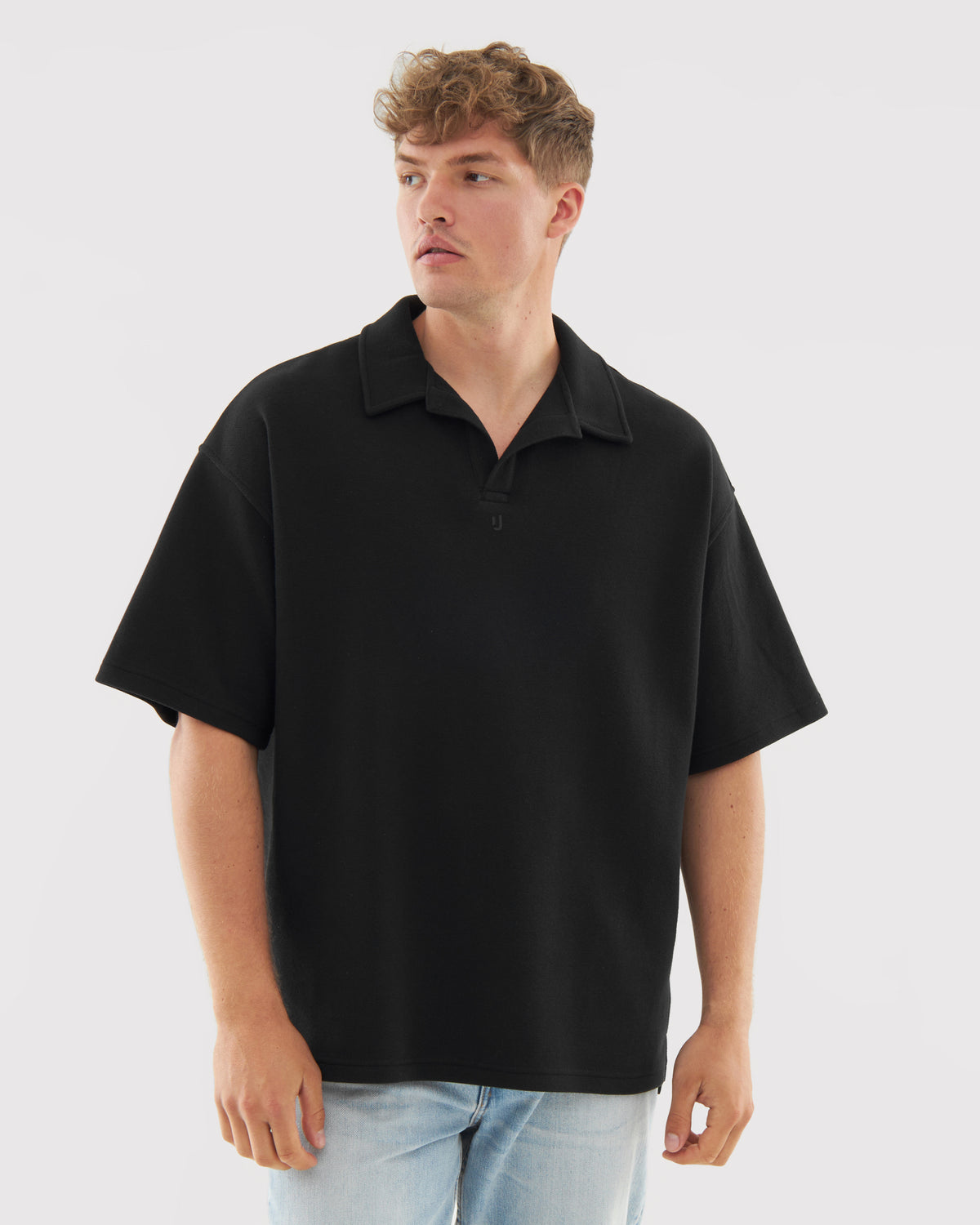 Mann trägt schwarzes Poloshirt mit kurzem Arm und offenem Kragen, dazu helle Jeans