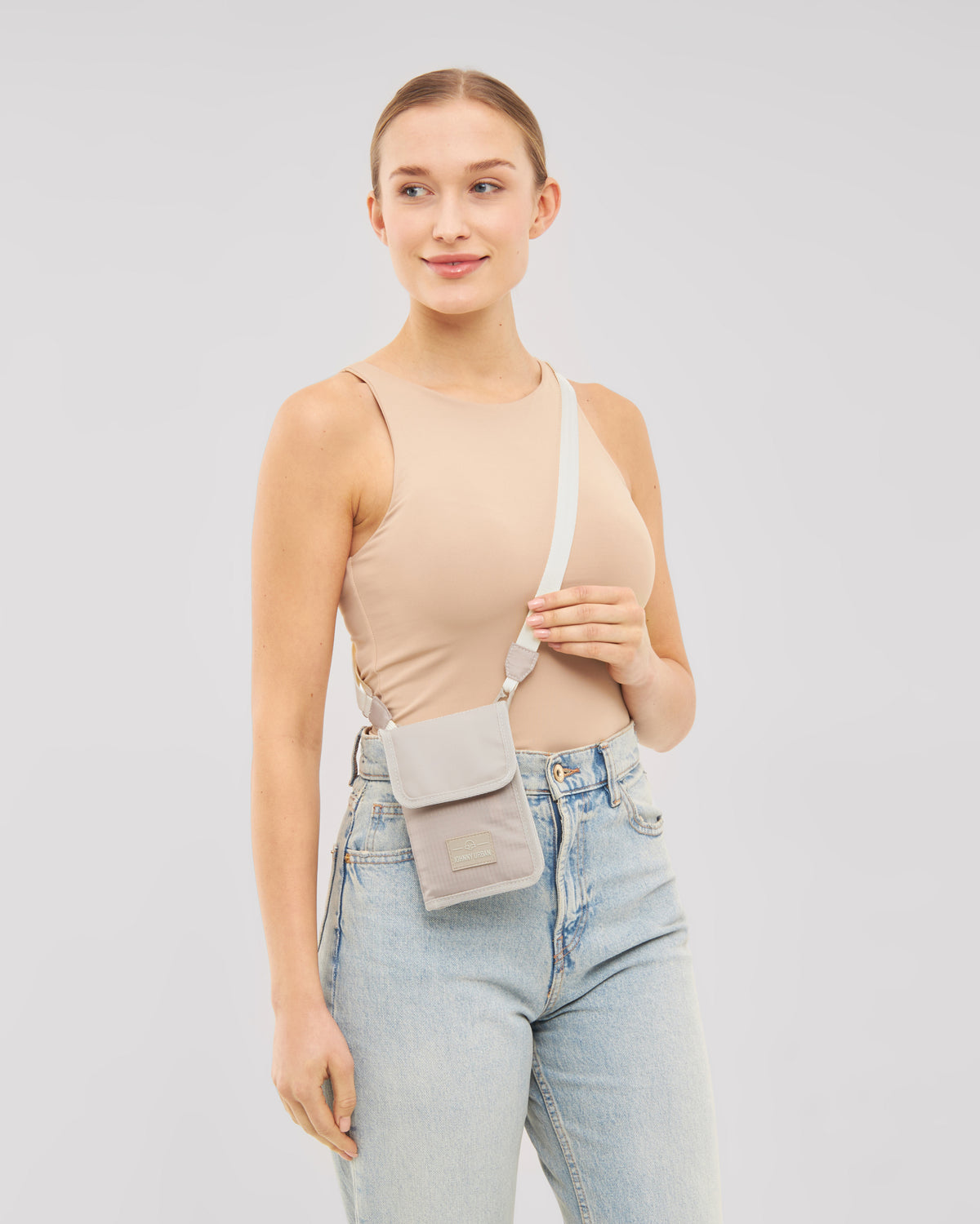Frau trägt das beige Portemonnaie 'Troy' mit Umhängeriemen kombiniert mit beigem Top und hellblauen Jeans