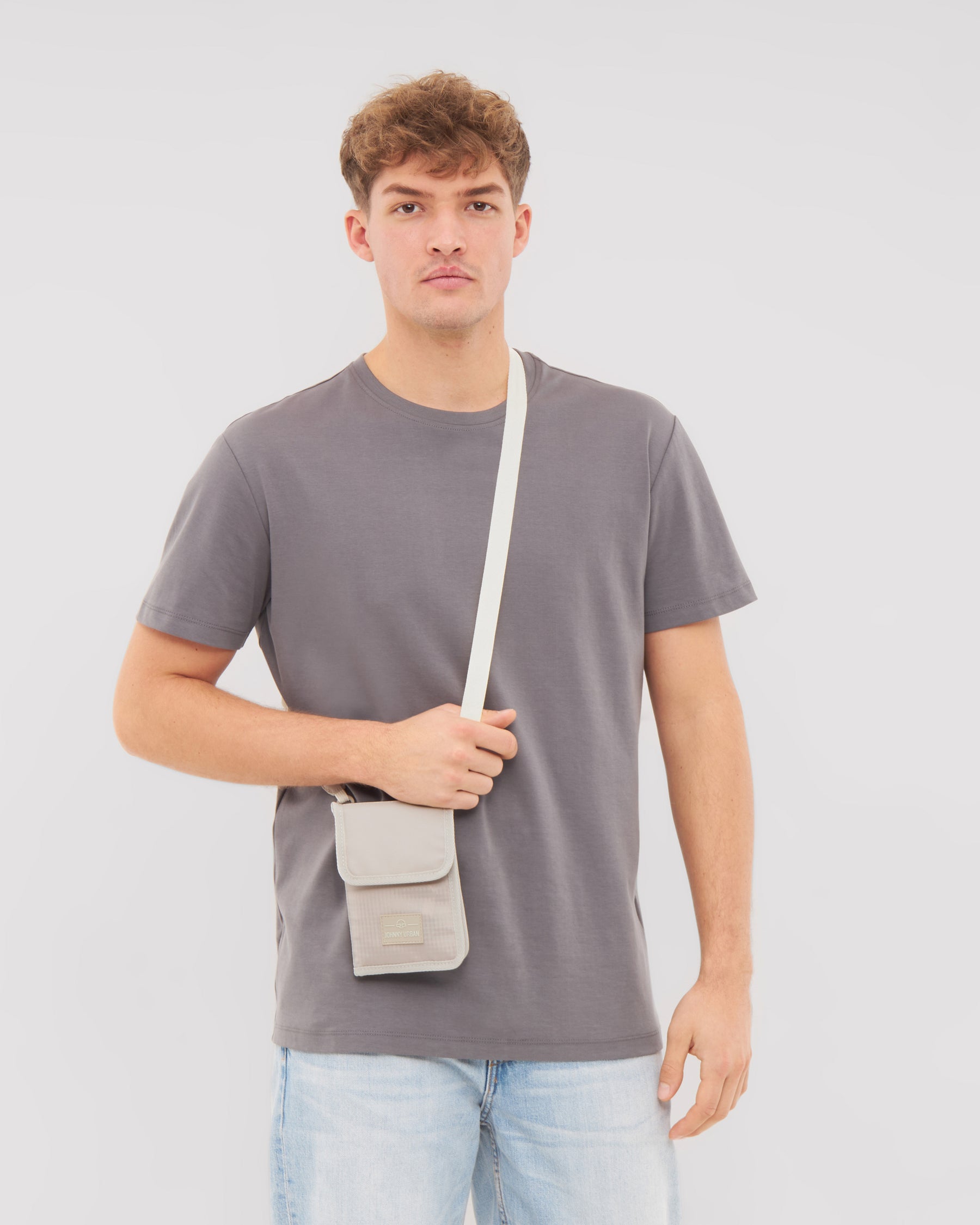 Junger Mann trägt beiges Portemonnaie 'Troy' zum Umhängen über grauem T-Shirt und hellen Jeans