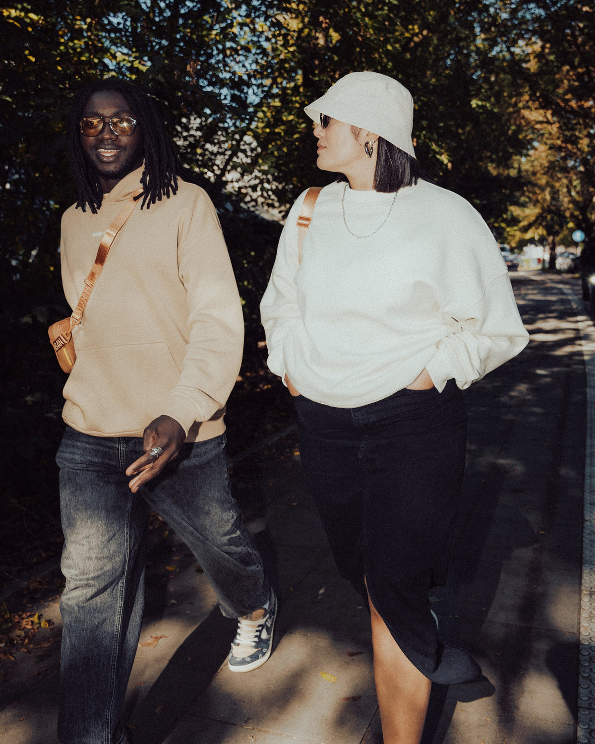 Zwei Menschen gehen draußen, eine trägt weißen oversized Crewneck 'Carter' Pullover, schwarze Jeans und Hut