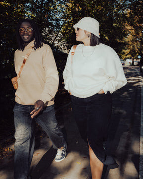 Zwei Menschen gehen draußen, eine trägt weißen oversized Crewneck 'Carter' Pullover, schwarze Jeans und Hut