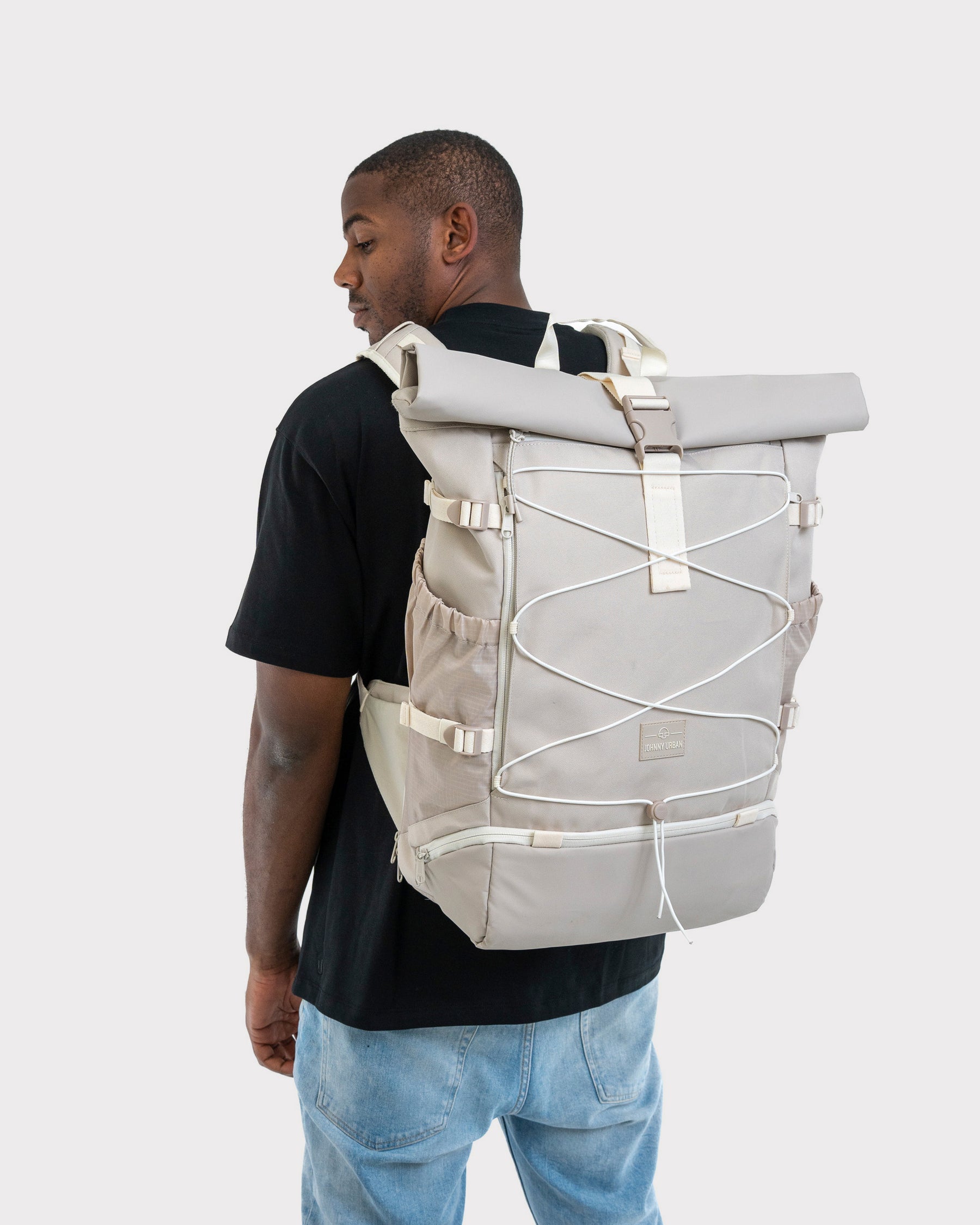 Mann mit schwarzem T-Shirt und Jeans trägt beigefarbenen Johnny Urban Reiserucksack 'Allen Large Travel' mit gerolltem Verschluss und elastischen Schnüren